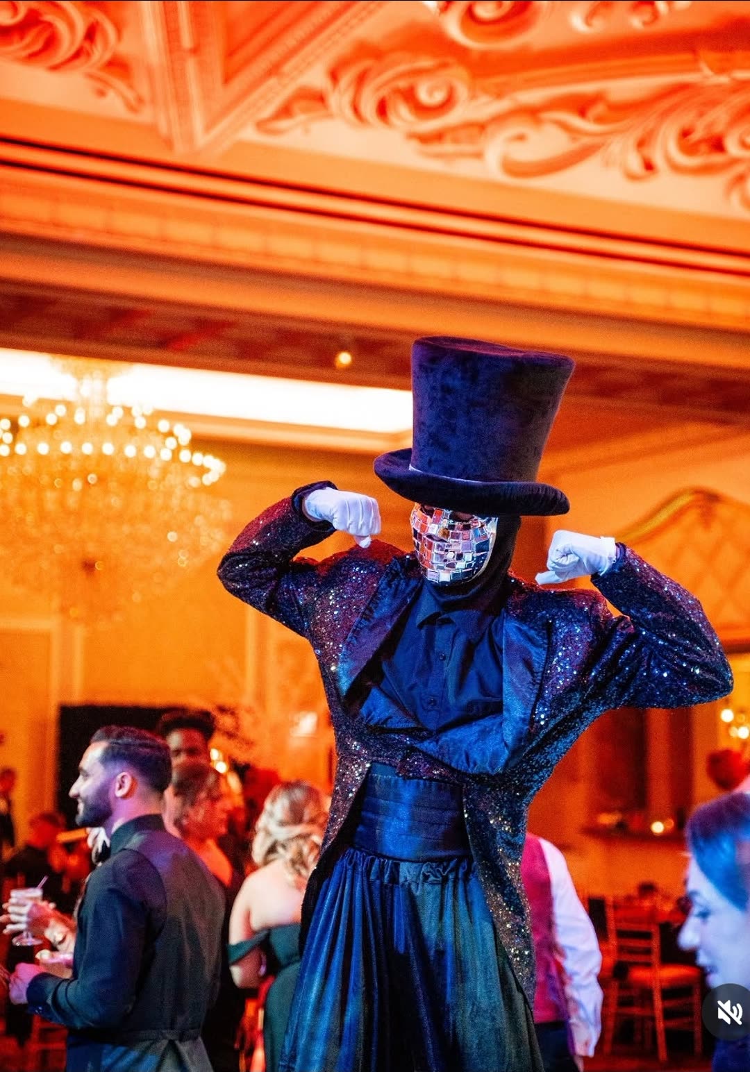 Stilt performer in a mirrored mask and top hat posing in an ornate ballroom
